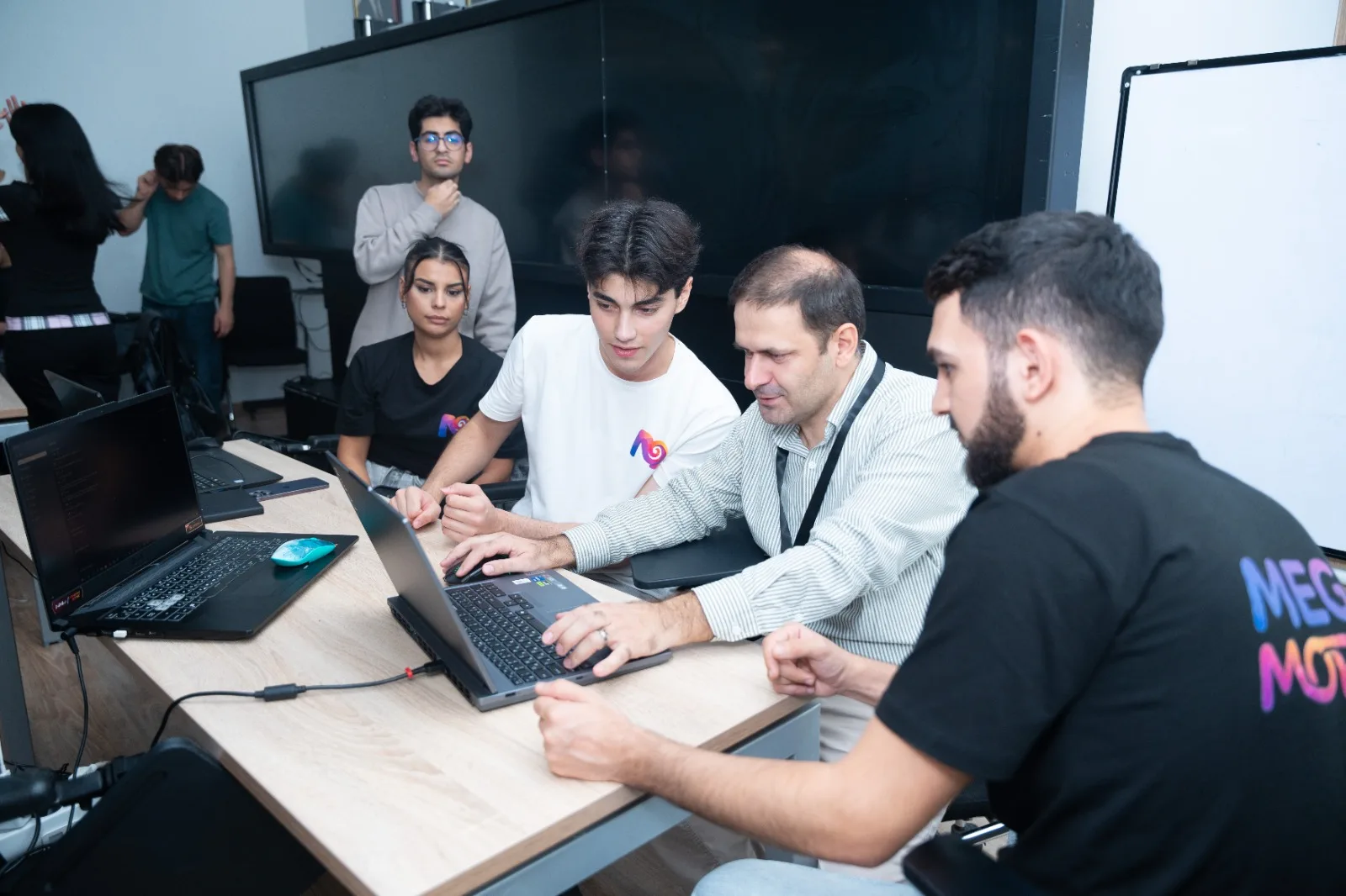 A mentor sitting with a team at their laptop at GameJamPlus Azerbaijan, teammates watching the screen