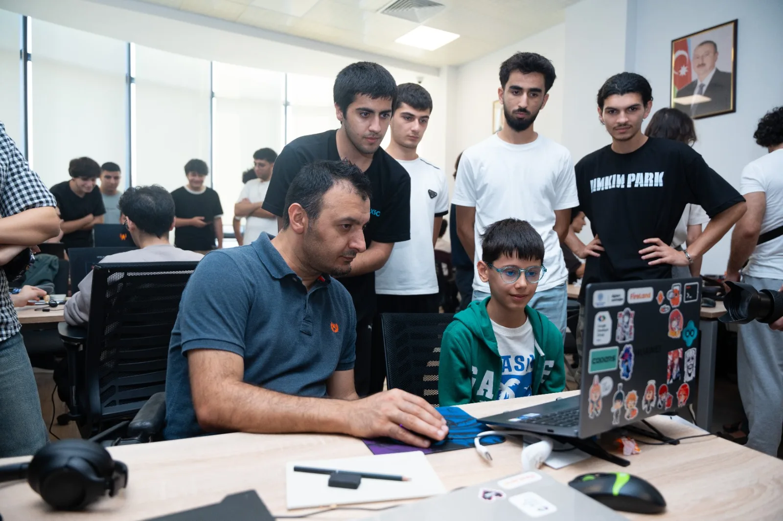 A game jam participant plays a submitted build while a crowd of other developers watches over his shoulder